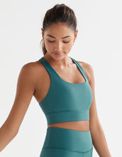 Woman wearing a teal sports bra and leggings on a white background