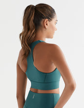Woman wearing a teal sports bra and leggings on a light gray background