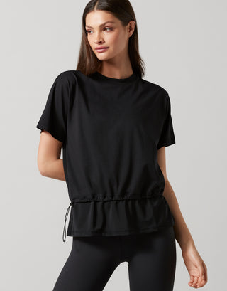A woman wearing a black, oversized, short-sleeved t-shirt with accent stripes and hardware on a model wearing black pants.
