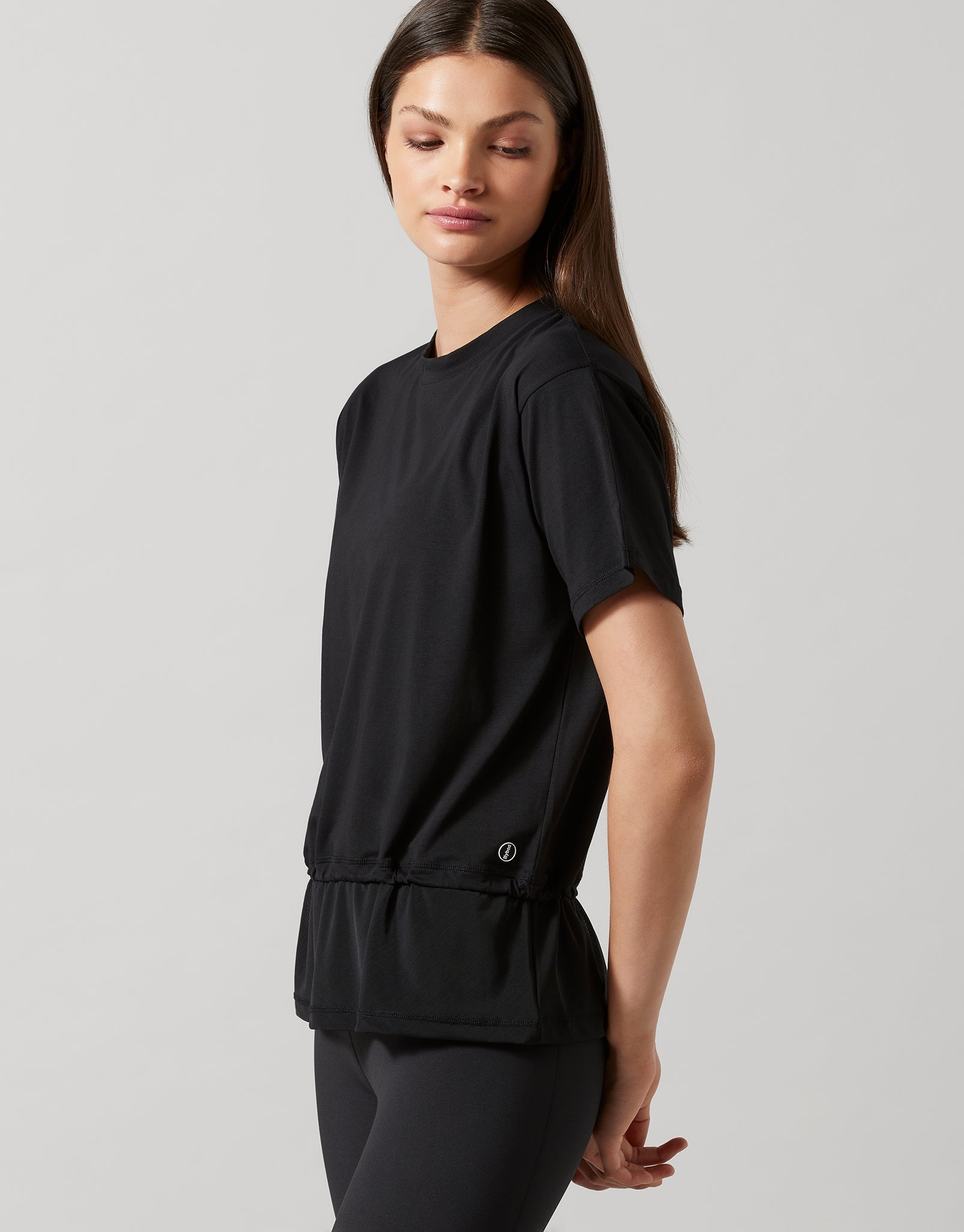 A model wearing a black, oversized, short-sleeved t-shirt with accent stripes and hardware on a model wearing black pants.