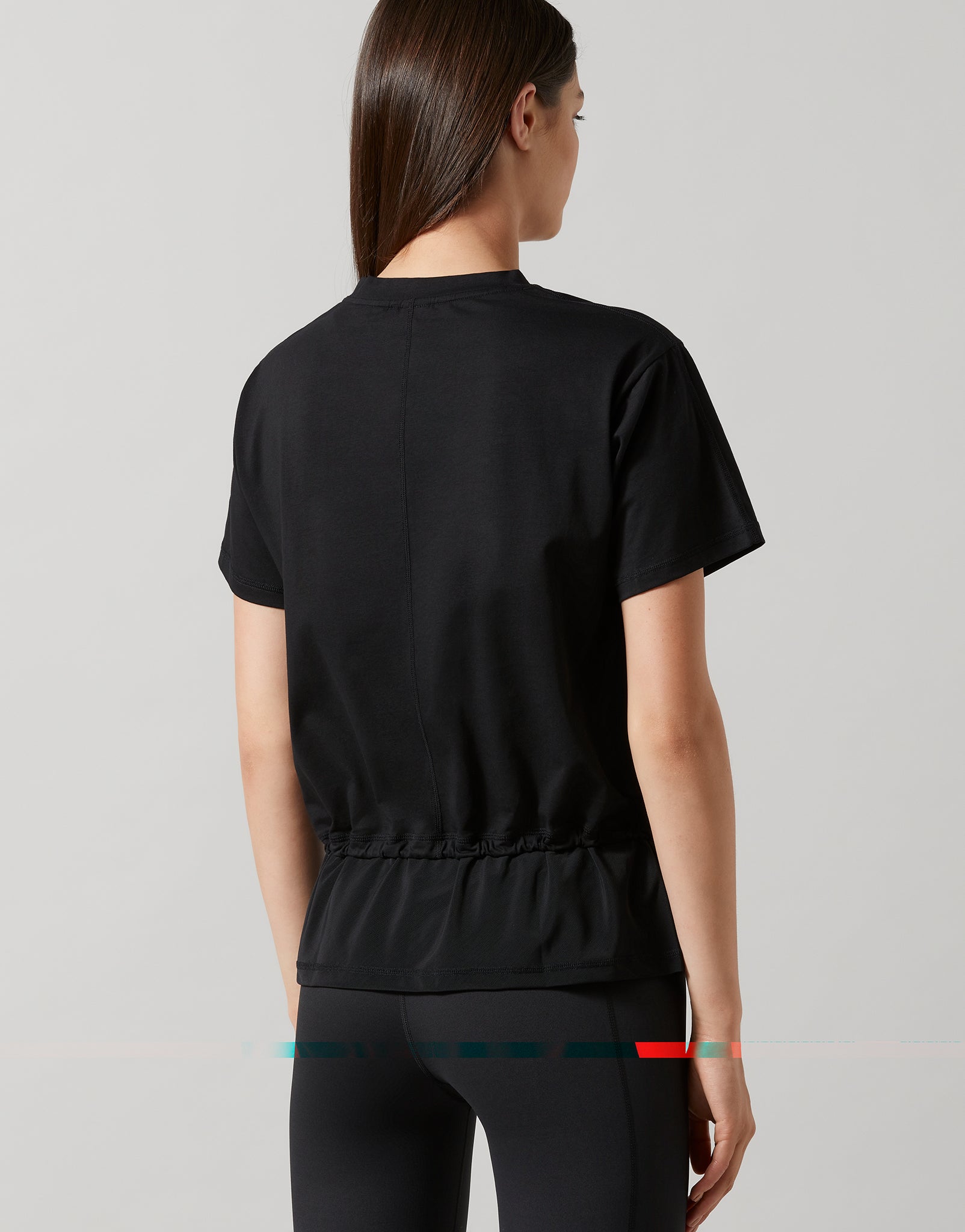 A woman wearing a black, oversized, short-sleeved t-shirt with accent stripes and hardware on a model wearing black leggings.