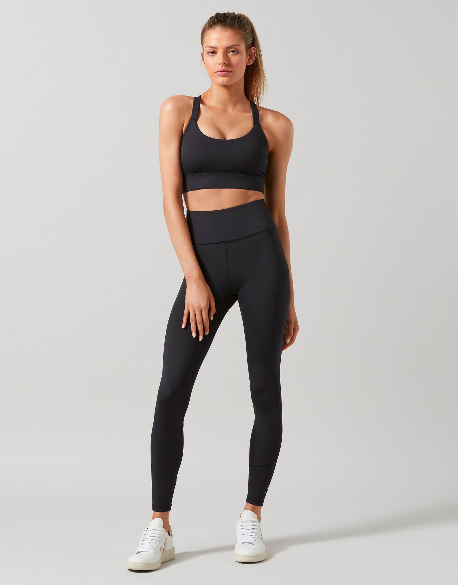 A model wearing full-length black Lilybod leggings that are high-waisted and made of recycled compression fabric.