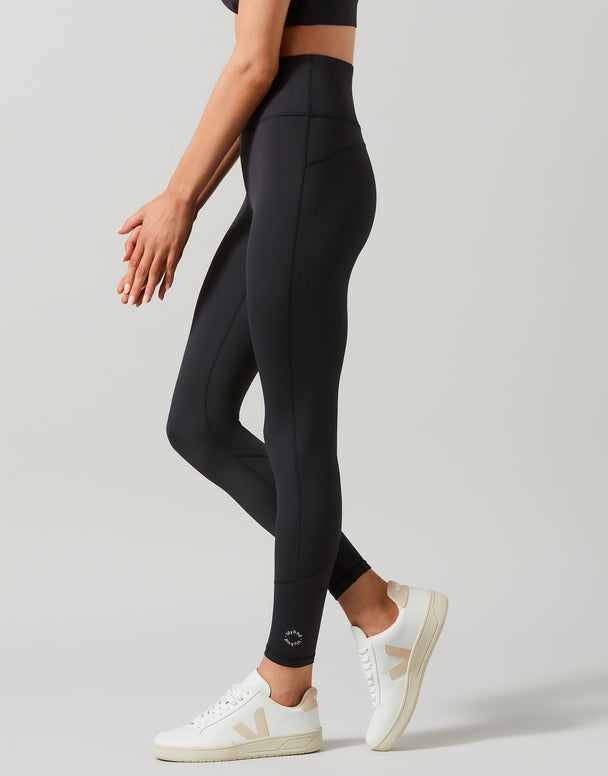 A woman wearing full-length black leggings that are high-waisted and made of recycled compression fabric.