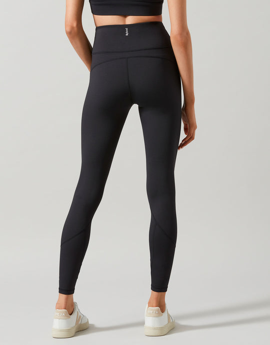 A model wearing full-length black leggings that are high-waisted and made of recycled compression fabric and white runners.