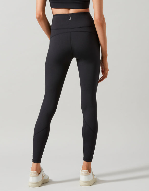 A model wearing full-length black leggings that are high-waisted and made of recycled compression fabric and white runners.
