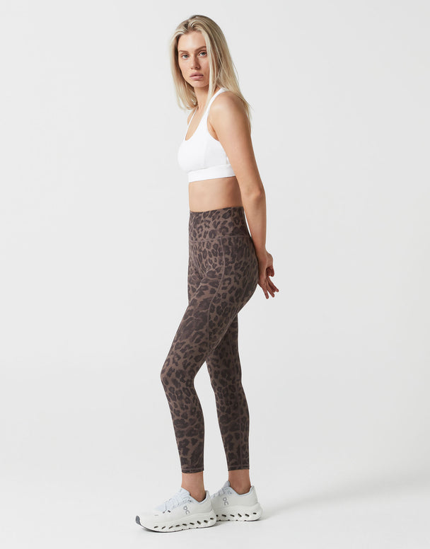 Woman wearing a white sports bra and leopard print leggings on a white background