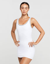 Woman wearing a white tank dress with black trim on a plain background