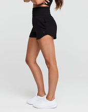 Person wearing black athletic shorts and white sneakers on a light gray background