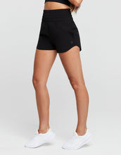 Person wearing black shorts and white sneakers on a plain background