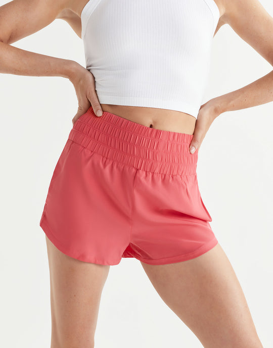 Person wearing coral shorts and a white top on a light gray background