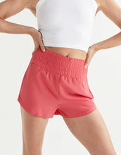 Person wearing coral shorts and a white top on a light gray background