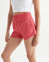Person wearing coral shorts and a white top on a light gray background