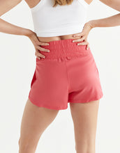 Person wearing pink shorts and a white top on a light gray background