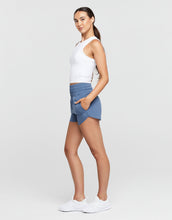 Woman wearing a white top and blue skirt on a plain background