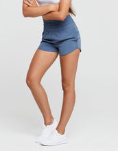 Person wearing blue shorts and white sneakers on a light gray background