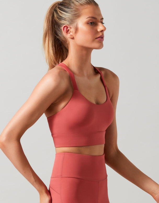 Woman wearing a coral sports bra and leggings on a light gray background