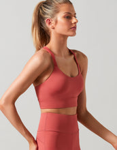Woman wearing a coral sports bra and leggings on a light gray background