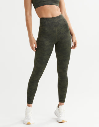 Person wearing green leggings and white sneakers on a plain background