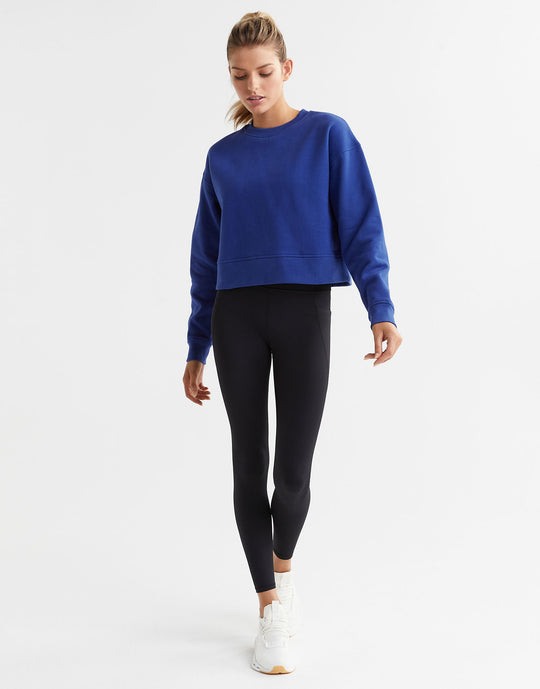 Woman wearing a blue sweatshirt and black leggings on a white background
