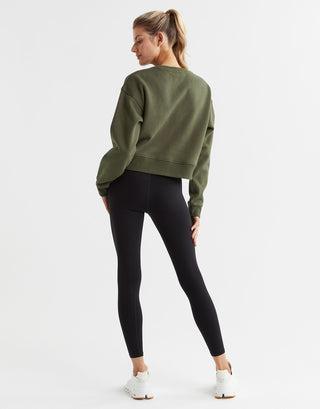 A woman wearing an olive green sweater and black leggings with white runners.