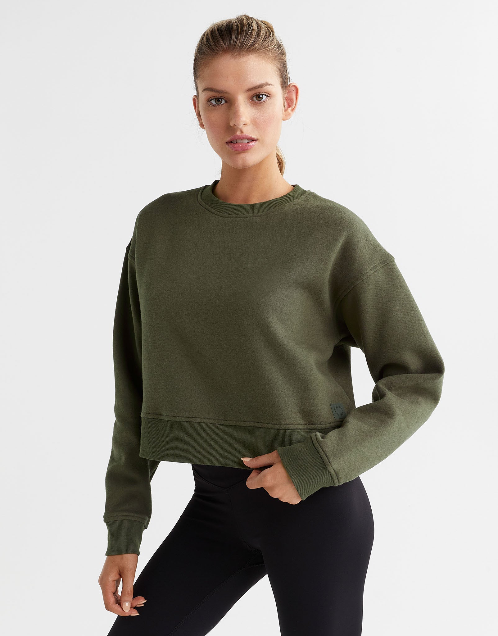 A woman wearing an olive green sweater and black leggings.