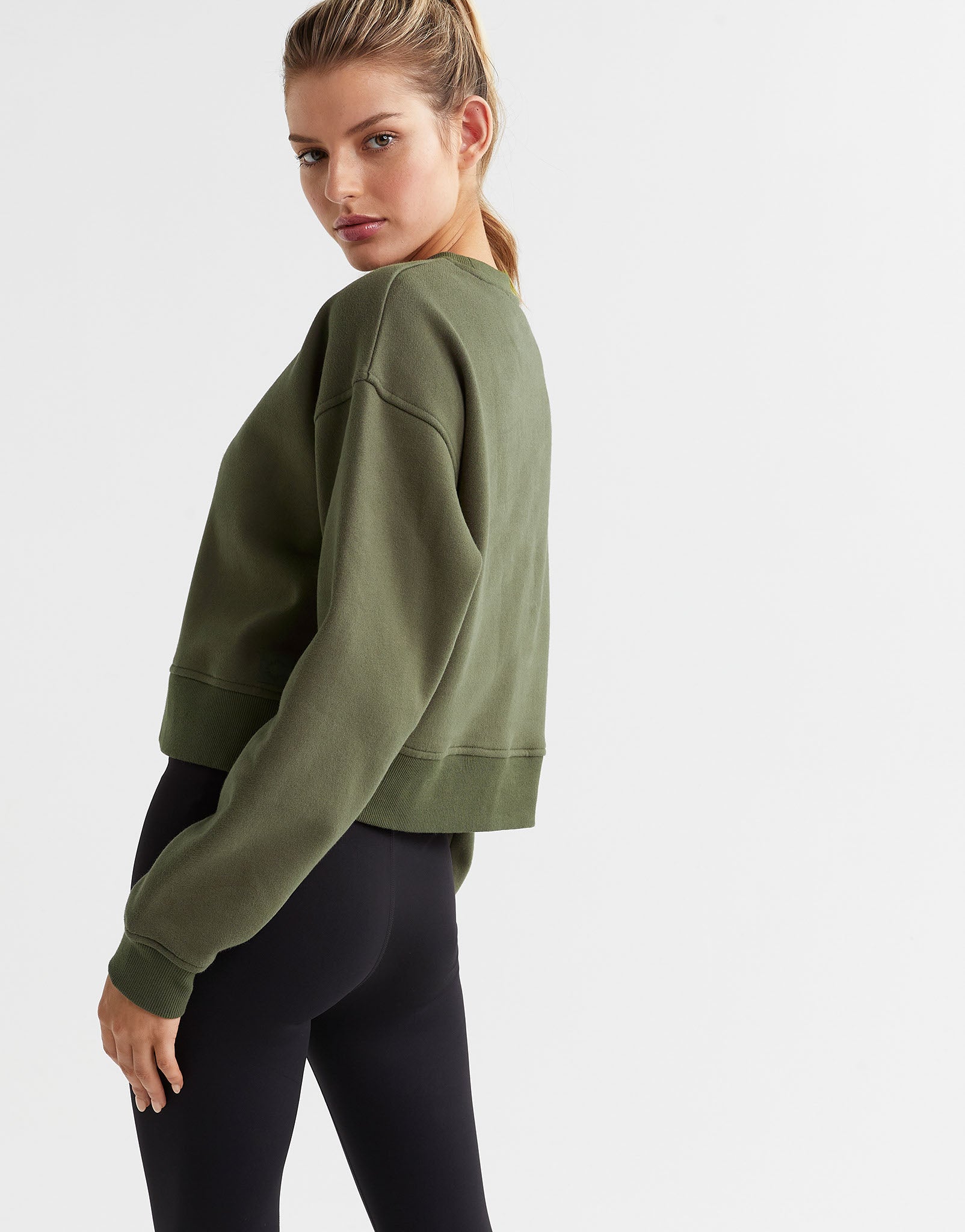 A woman wearing an olive green sweater and black leggings. Rear view.