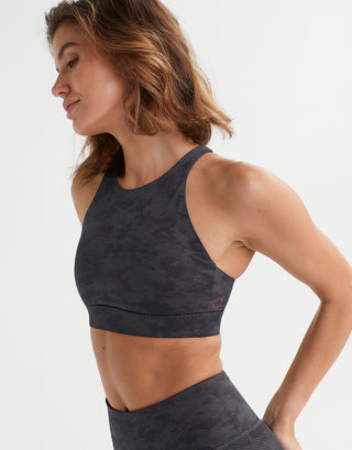 A woman wearing a dark gray patterned sports bra and matching high-waisted leggings, shown in a side profile against a clean white studio background.