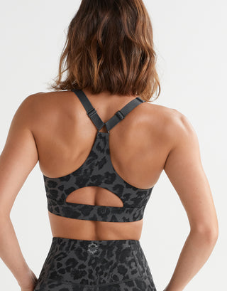 A rear view of a woman wearing a grey leopard print sports bra and leggings.