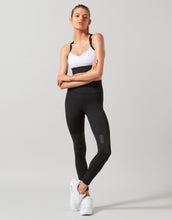 Woman wearing black leggings and a white sports bra on a gray background