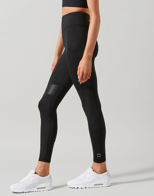Person wearing black leggings with white sneakers on a light gray background