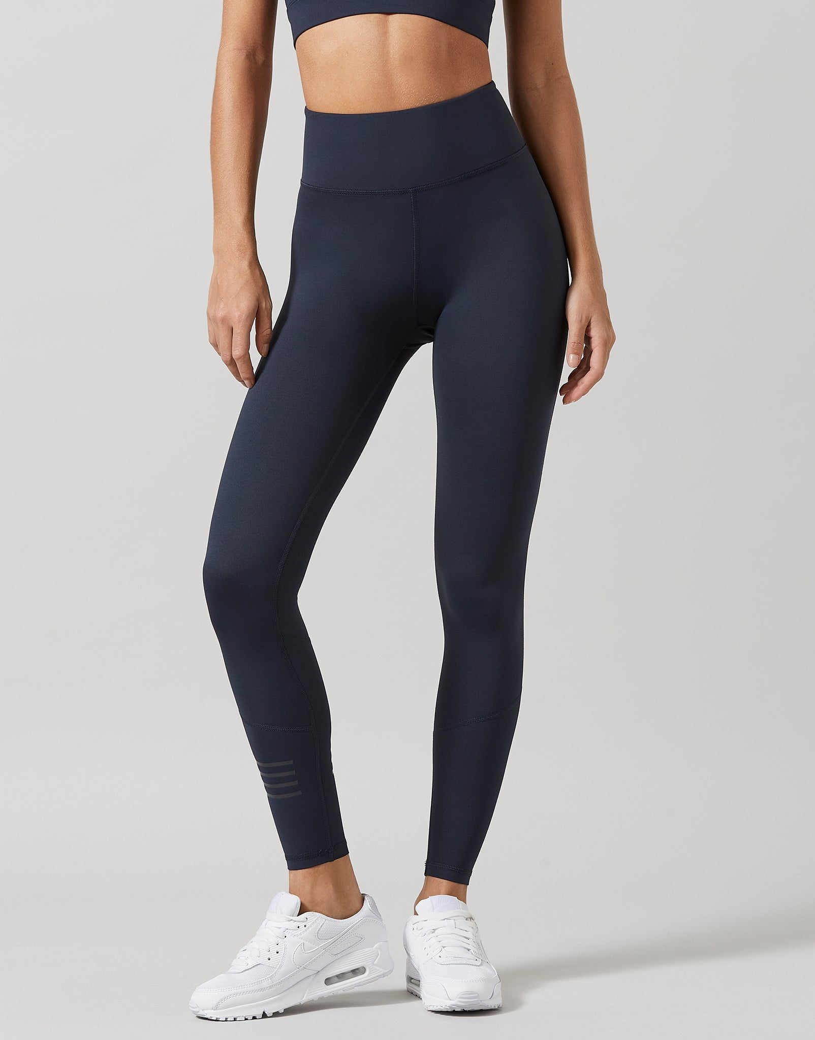 Person wearing navy leggings and white sneakers on a light gray background