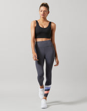 Woman wearing a black sports bra and gray leggings on a light gray background