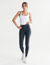 Woman wearing a white tank top and navy leggings with white stripes on a white background