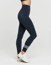 Woman wearing navy leggings with white stripes on a light gray background