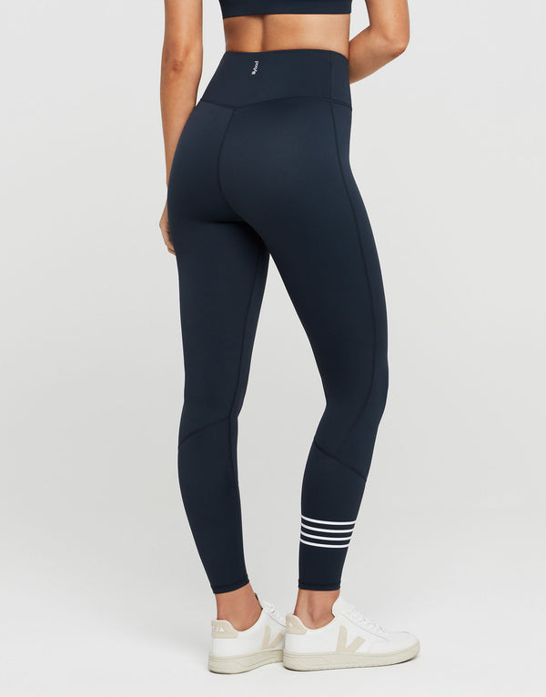 Woman wearing navy blue leggings with white stripes on a light gray background