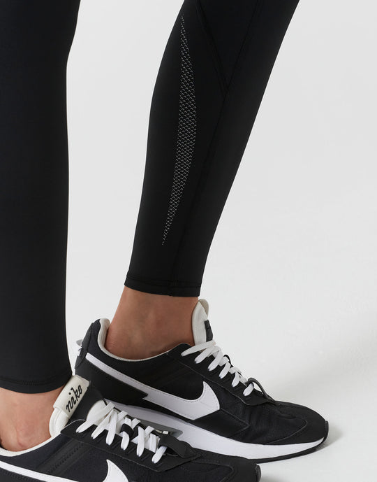 Black athletic shoes with white accents worn with black leggings on a light gray background