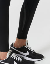 Black athletic shoes with white accents worn with black leggings on a light gray background