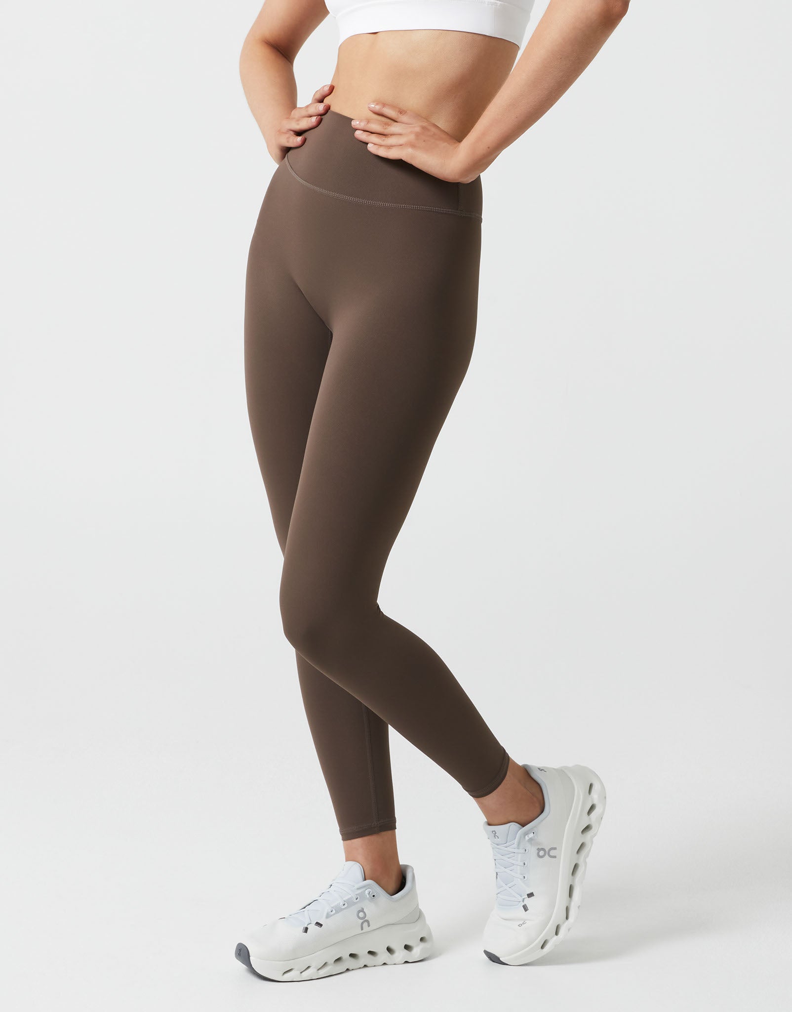 Person wearing brown leggings and white sneakers on a white background