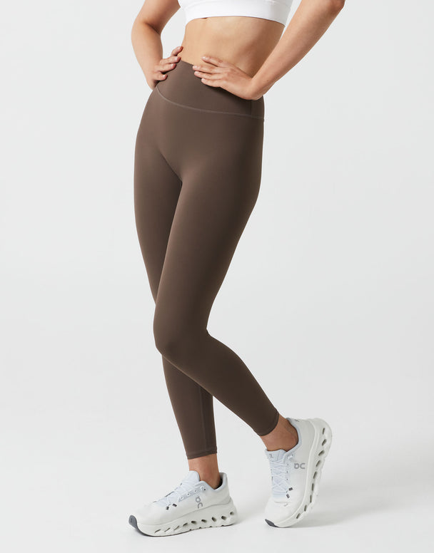 Person wearing brown leggings and white sneakers on a white background