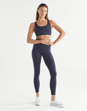 Woman wearing a navy blue sports bra and leggings set on a white background