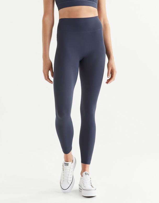 Woman wearing navy blue sports leggings and white sneakers on a white background