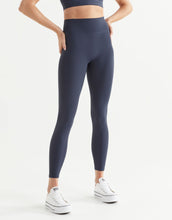 Woman wearing navy leggings and white sneakers on a white background