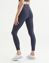 Woman wearing navy blue leggings and runners on a white background