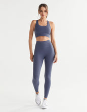 Woman wearing a matching purple sports bra and leggings set on a white background