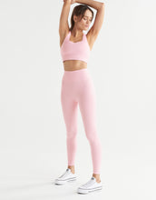 A woman wearing pink leggings and a sports bra on a white background.