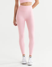 A woman wearing powder pink full-length leggings and white sneakers.