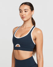 Woman wearing a navy sports bra with white accents on a light gray background