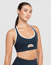Woman wearing a navy sports bra with white accents on a light gray background