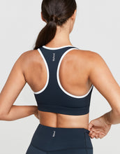 Person wearing a navy sports bra with white accents on a light gray background
