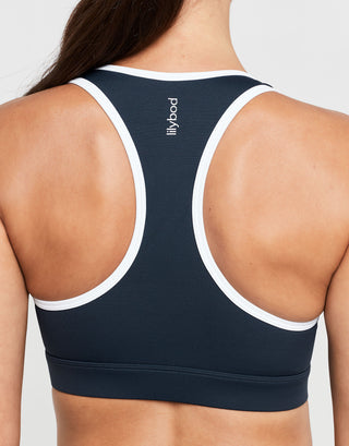 Navy sports bra with white straps on a model against a light gray background